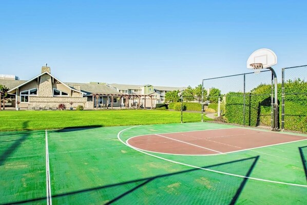 An outdoor basketball court with a green surface, a basketball hoop, and a fence. - Oceanfront 2BR 3rd-Floor | Balcony | Pool (Westport)