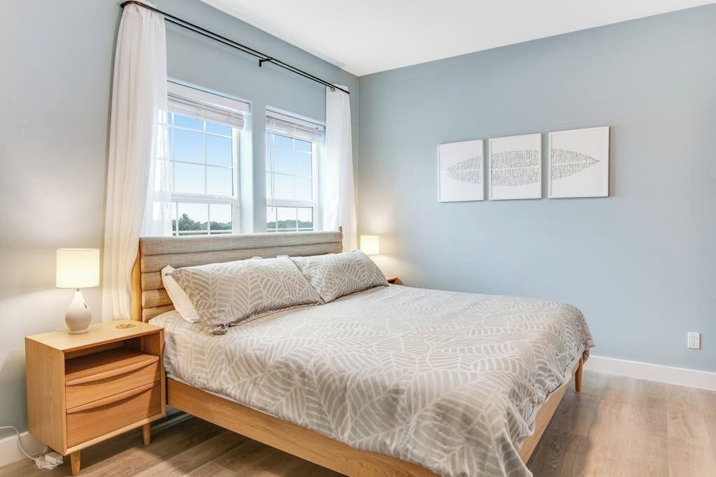 Un dormitorio con una cama, mesita de noche, lámpara y tres cuadros en la pared.