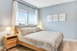 Une chambre à coucher avec un lit, une table de chevet, une lampe et trois tableaux encadrés accrochés au mur.