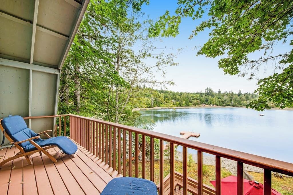 A wooden deck with a view of a lake, surrounded by trees.
