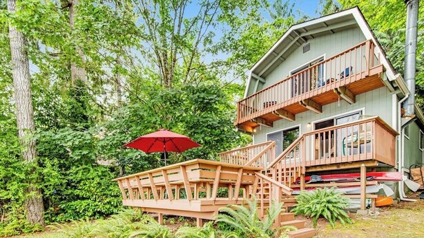 A two-story wooden cabin with a balcony, surrounded by lush greenery. - 1BR Soundview Dog Friendly - Dock - WoodStove (Shelton)