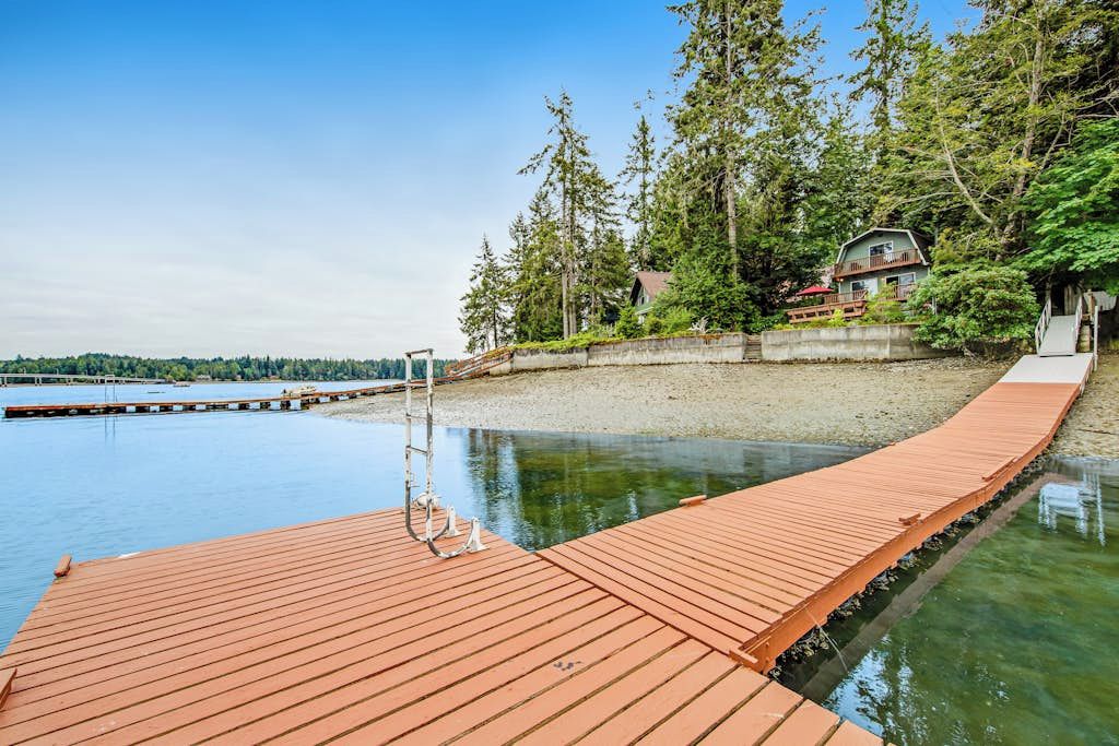 A wooden dock extending into calm water, surrounded by dense trees and a distant shoreline.