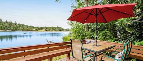 Une terrasse en bois avec une table et des chaises, un parasol rouge et une vue sur un lac.
