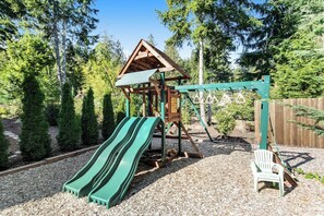 Ein Spielplatz mit Rutsche und Schaukeln, umgeben von Bäumen.