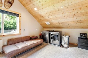 Une pièce avec un plafond en pente, un canapé, un coin cuisine équipé d’une cuisinière et une fenêtre donnant sur un paysage verdoyant.