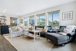 A modern living room with a sofa, a coffee table, and a kitchen area in the background. - 3BR Oceanview - Balcony - Firepit - Washer Dryer (Pacific Beach)