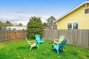 A residential backyard with a wooden fence, a yellow house, and three Adirondack chairs. - 3BR Oceanview - Balcony - Firepit - Washer Dryer (Pacific Beach)