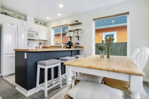 A modern kitchen with white cabinetry, a wooden island, and bar stools. - 3BR Oceanview - Balcony - Firepit - Washer Dryer (Pacific Beach)
