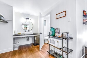 Une salle de bain moderne avec un meuble-lavabo blanc, un miroir rond et un panneau indiquant un espace dédié aux boissons chaudes.