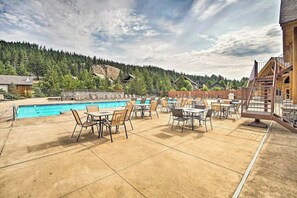 An outdoor pool area with lounge chairs and tables, surrounded by a wooden deck and overlooking a forested hillside. - 2BR mountainview condo with balcony & pool (Ronald)