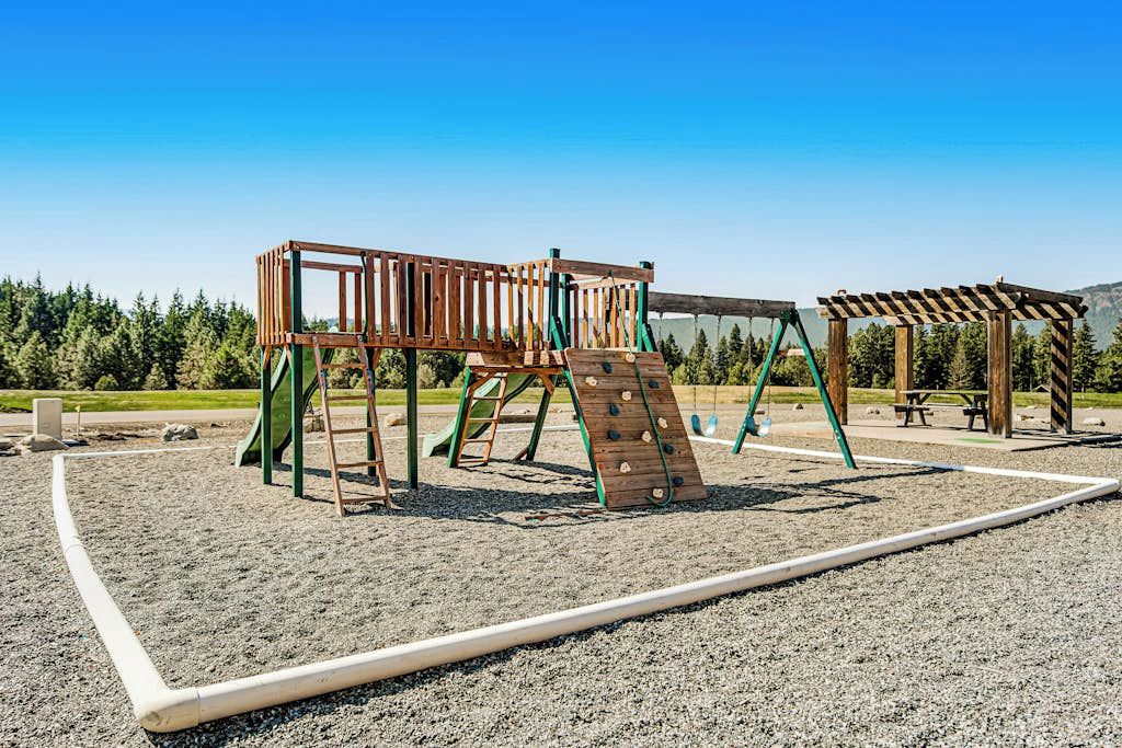 Ein Spielplatz mit einer hölzernen Kletteranlage und Schaukeln.