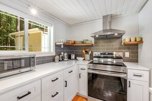 Cozinha moderna com armários brancos, eletrodomésticos de aço inoxidável e vista para o exterior.