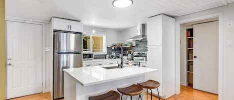 A modern kitchen with a central island, stainless steel appliances, and wooden bar stools.