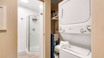 A laundry room with a front-loading washer and dryer, a glass shower enclosure, and a storage area with hanging clothes.