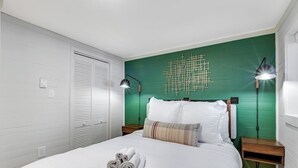 Una cama bien hecha con toallas enrolladas, una pared de acento verde y dos lámparas de noche.