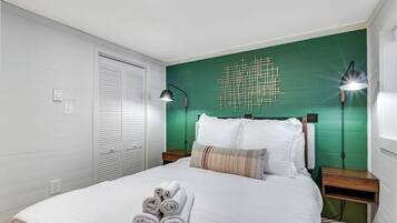 A neatly made bed with rolled towels, a green accent wall, and two bedside lamps.