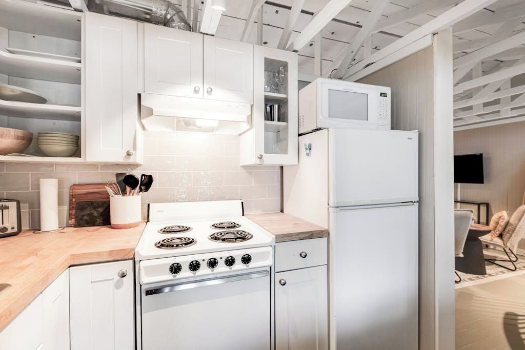 A modern kitchen with white cabinetry, a stove, a microwave, and a refrigerator.