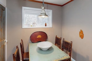 A dining area with a table, chairs, a bowl, a window with a view, and a hanging light fixture.