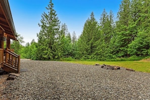 A gravel driveway leading to a wooden building with a porch, surrounded by dense green forest.