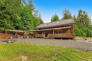 A wooden cabin with a porch, surrounded by trees and a gravel driveway.