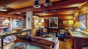 Interior acolhedor de uma cabana com teto de madeira, um sofá, uma mesa de jantar e várias luminárias.
