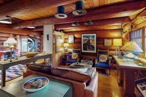 Interior acogedor de una cabaña con techo de madera, un sofá, una mesa de comedor y varias lámparas.