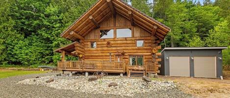 A log cabin with a porch, a garage, and a gravel driveway.