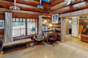 Interior d'una cabana de fusta amb un escriptori de fusta, una cadira, una banca i un piano.