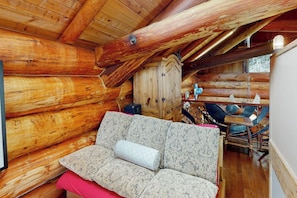 A log cabin interior with a sofa, wooden walls, and a dining area.
