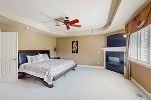 Ein Schlafzimmer mit einem Bett, einem Deckenventilator, einem Kamin und einem Fenster mit Vorhängen.