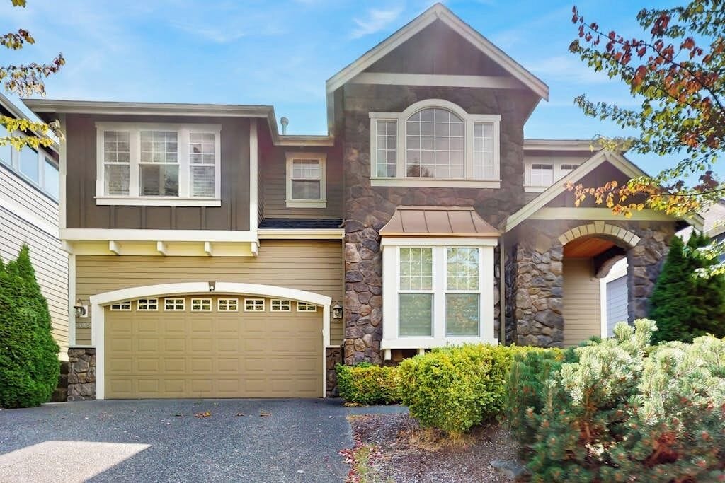A two-story house with a garage, stone facade, and a well-maintained front yard.