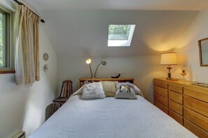 A bedroom with a skylight, a bed with pillows, a wooden dresser, a chair, and a bedside table with a lamp. - Relaxing 3BR Dog Friendly - WoodStove - Deck (Bainbridge Island)