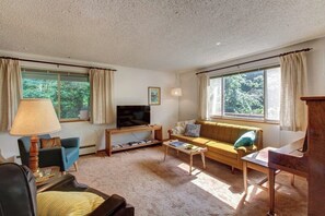 A living room with a sofa, television, and a table. - Relaxing 3BR Dog Friendly - WoodStove - Deck (Bainbridge Island)