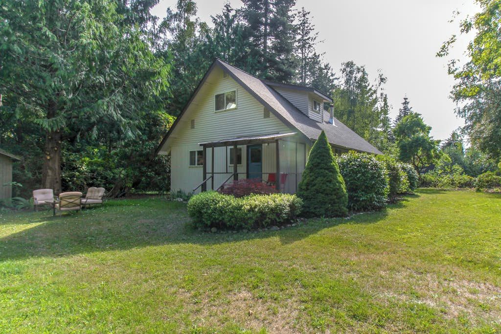 Ein eingeschossiges Haus mit geneigtem Dach, einer überdachten Veranda und einem gepflegten Rasen.