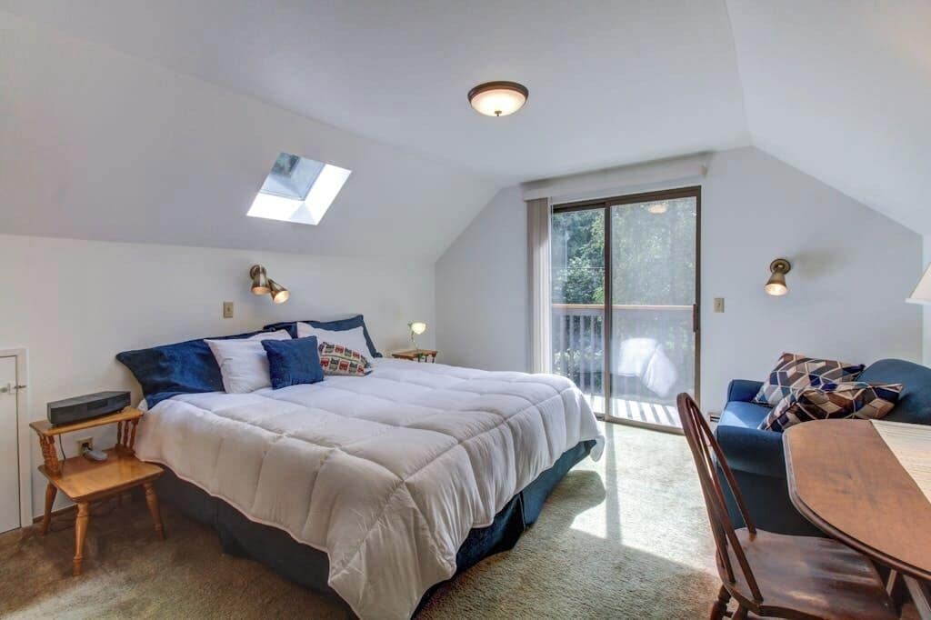 Ein Schlafzimmer mit einem großen Bett, einem Schreibtisch, einem Stuhl und einem Fenster mit Blick auf Grünflächen.
