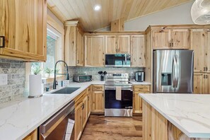 A modern kitchen with wooden cabinets, stainless steel appliances, and a marble countertop. - 3 BR Cozy Mountain Getaway, New Build (Ronald)