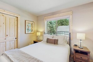 A bedroom with a bed, two bedside tables, a window with a view of trees, and a door. - 3 BR Cozy Mountain Getaway, New Build (Ronald)
