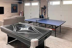 A ping pong table in a garage with a dartboard and sports equipment in the background. - 3 BR Cozy Mountain Getaway, New Build (Ronald)
