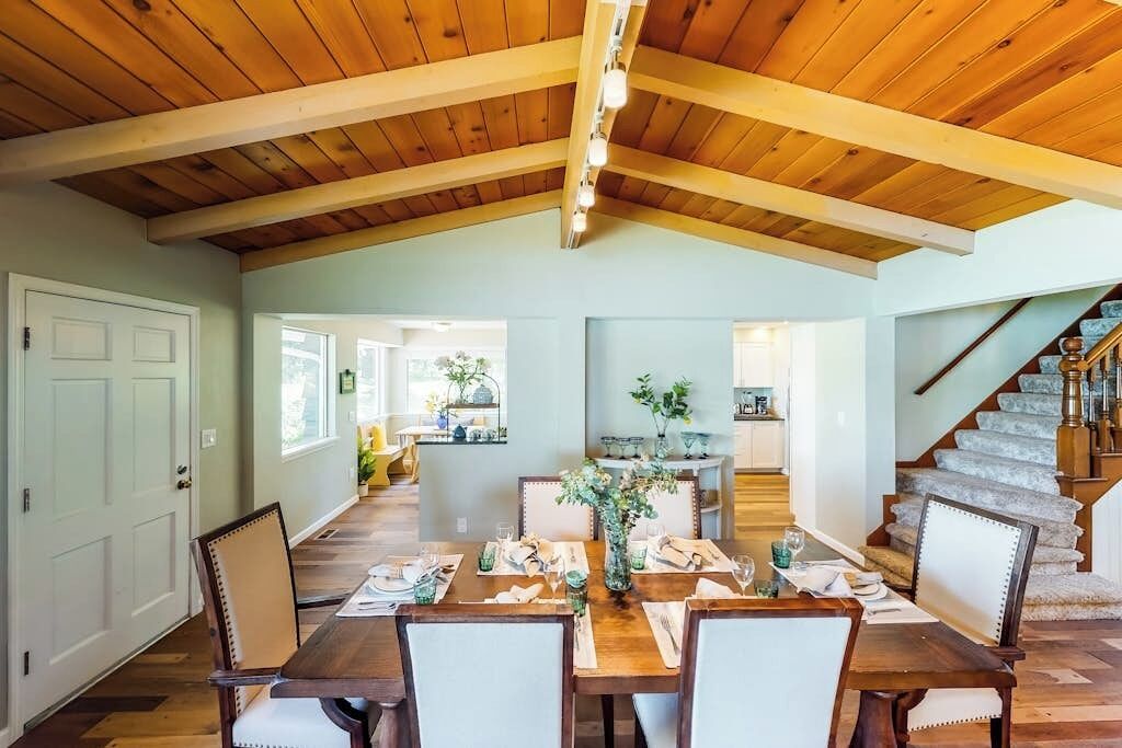 A dining area with a wooden ceiling, a staircase, and a view into the kitchen.