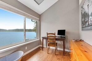 Ein Zimmer mit Schreibtisch, Stuhl und einem großen Fenster mit Blick auf ein Gewässer.