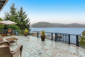 Eine Terrasse mit Gartenmöbeln, Geländer und Blick auf ein Gewässer und entfernte Landschaft.