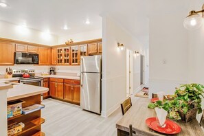 Cocina moderna con armarios de madera, electrodomésticos de acero inoxidable y una zona de comedor con una mesa dispuesta para dos.