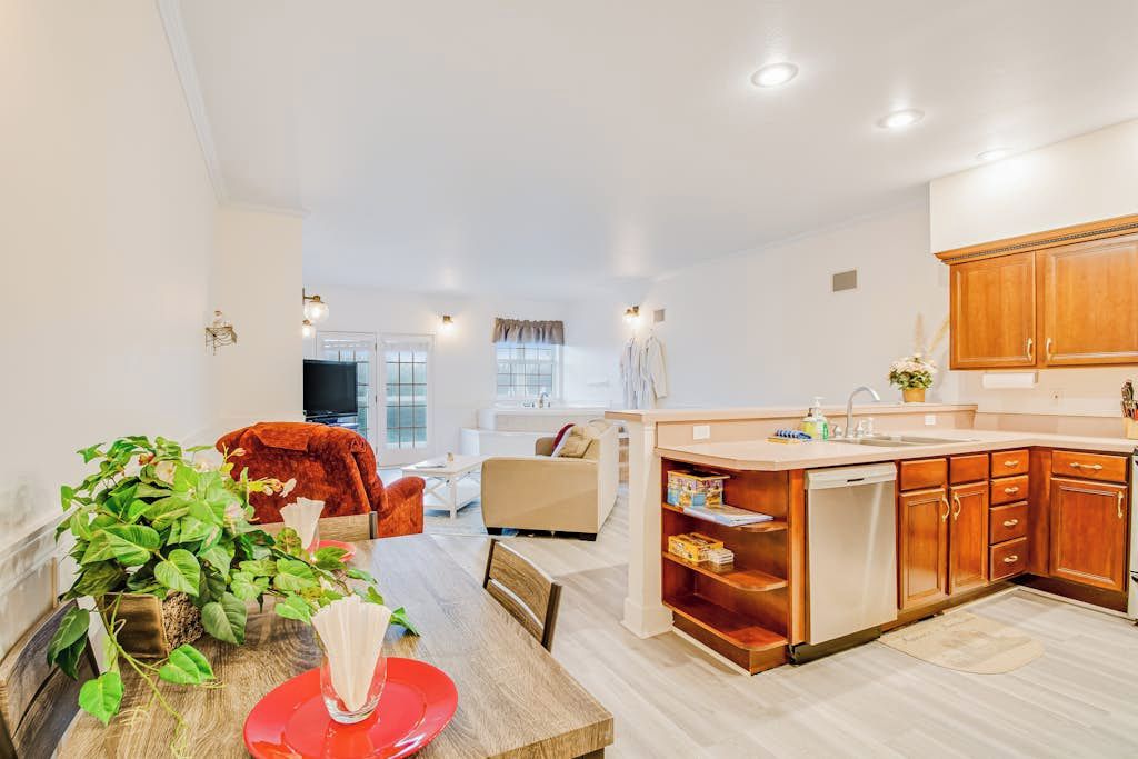 Une cuisine moderne avec des meubles en bois, un coin repas doté d’une table rouge et un salon avec un canapé et un téléviseur.