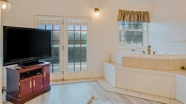 Ein Zimmer mit Fernseher auf einer Holzkommode, einem großen Fenster mit Ausblick und einer Badewanne mit Fenster davor.