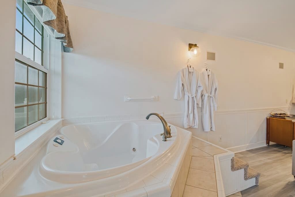 Une salle de bain moderne avec une grande baignoire sur pieds, une fenêtre offrant une belle vue et un ensemble de peignoirs blancs posés sur un porte-serviettes.