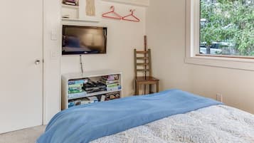 A bedroom with a bed, a television mounted on the wall, a bookshelf, and a window with a view of trees.