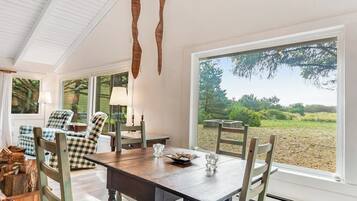 A dining area with a wooden table and chairs, large windows, and a view of the outdoors.