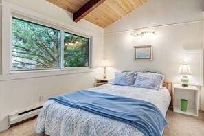 Une chambre à coucher avec un lit, deux lampes de chevet, un tableau encadré au mur et une fenêtre donnant sur des arbres.