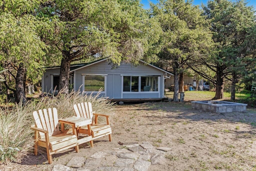 A small cabin with a stone patio, two Adirondack chairs, and a surrounding wooded area.