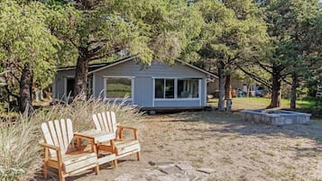 A small cabin with a stone patio, two Adirondack chairs, and a surrounding wooded area.